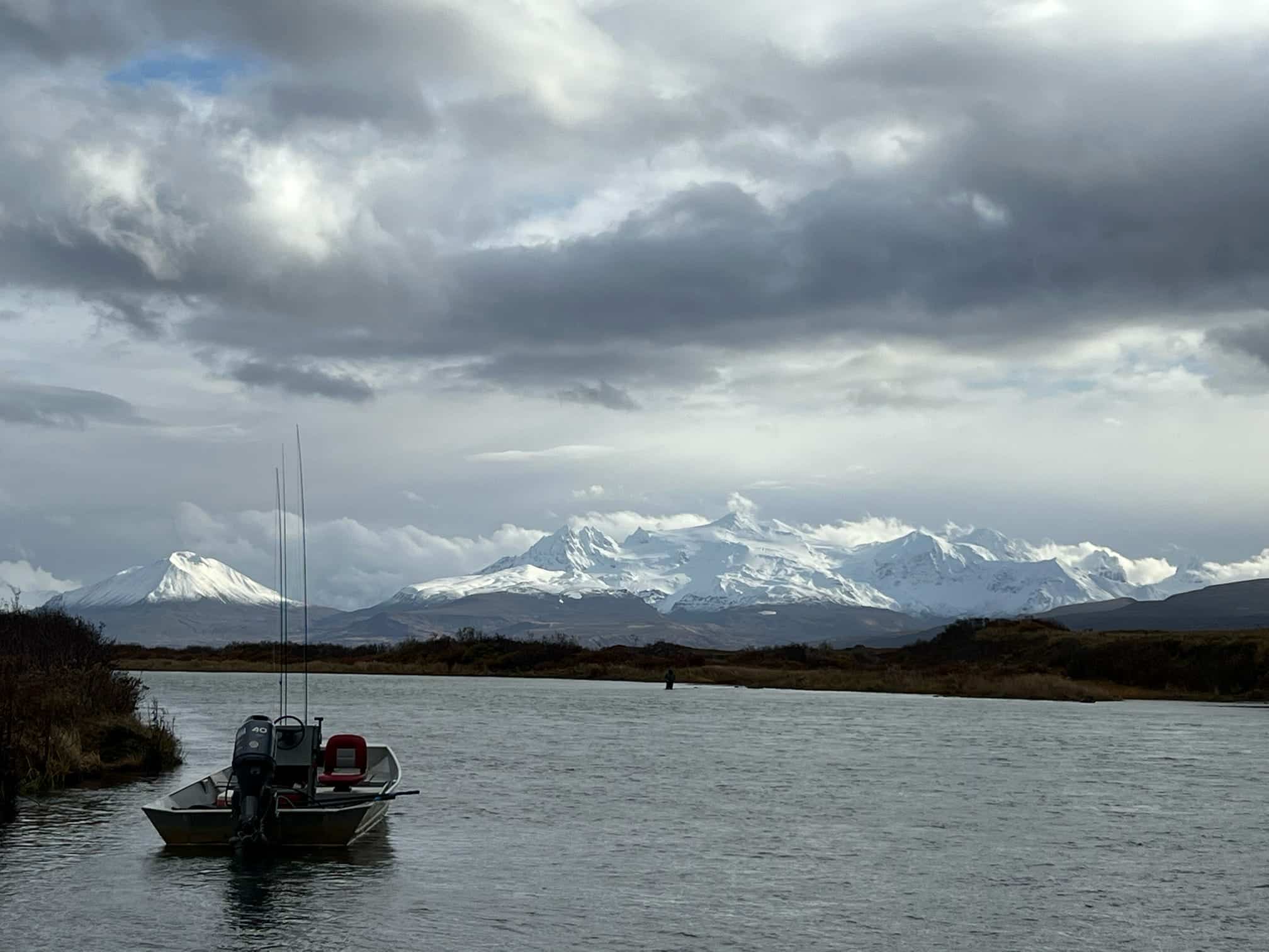 Alaska river with fishing boat and snow-capped mountains in the distance