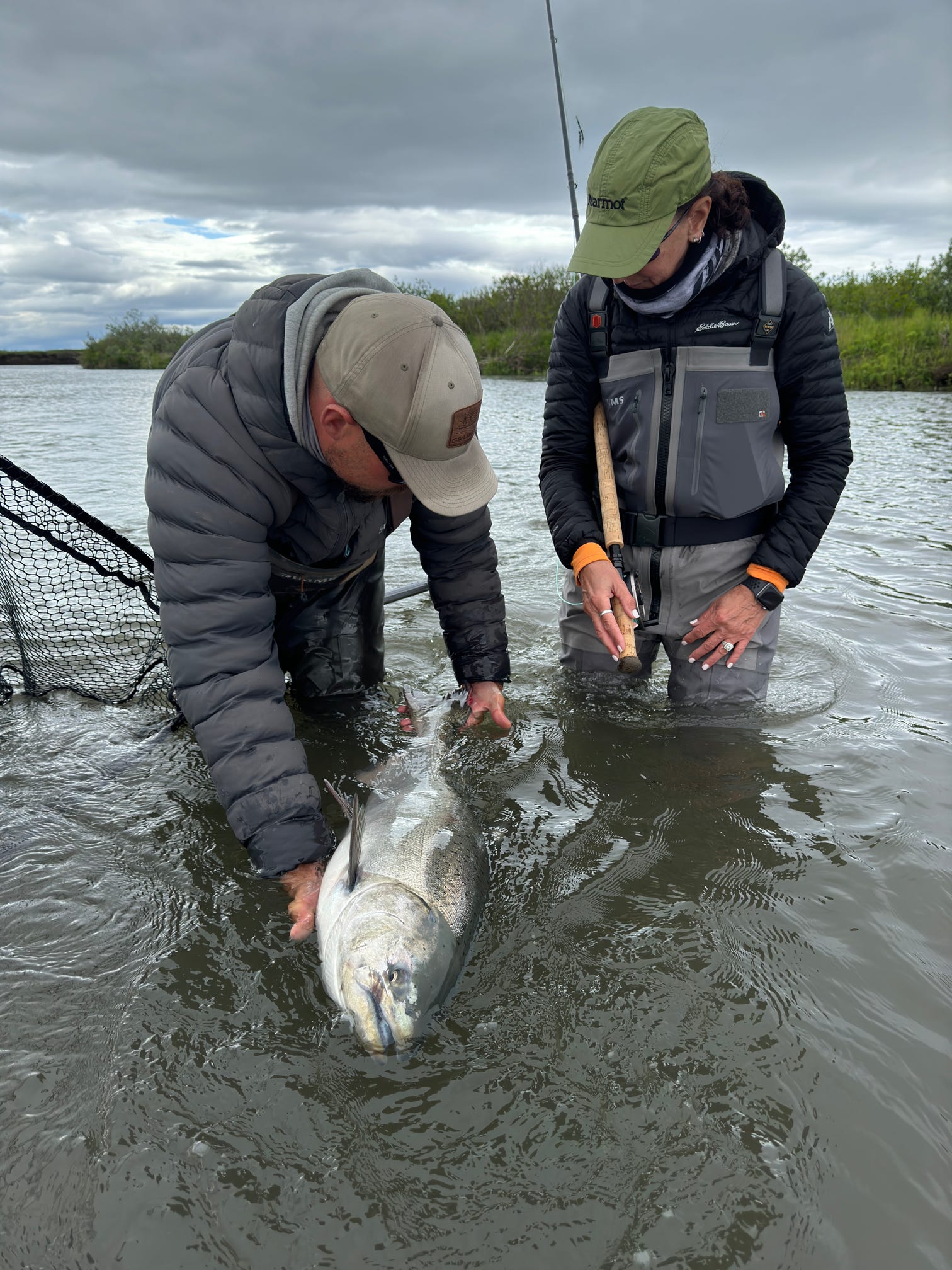 Anglers in waders release a large salmon back into the river in Alaska