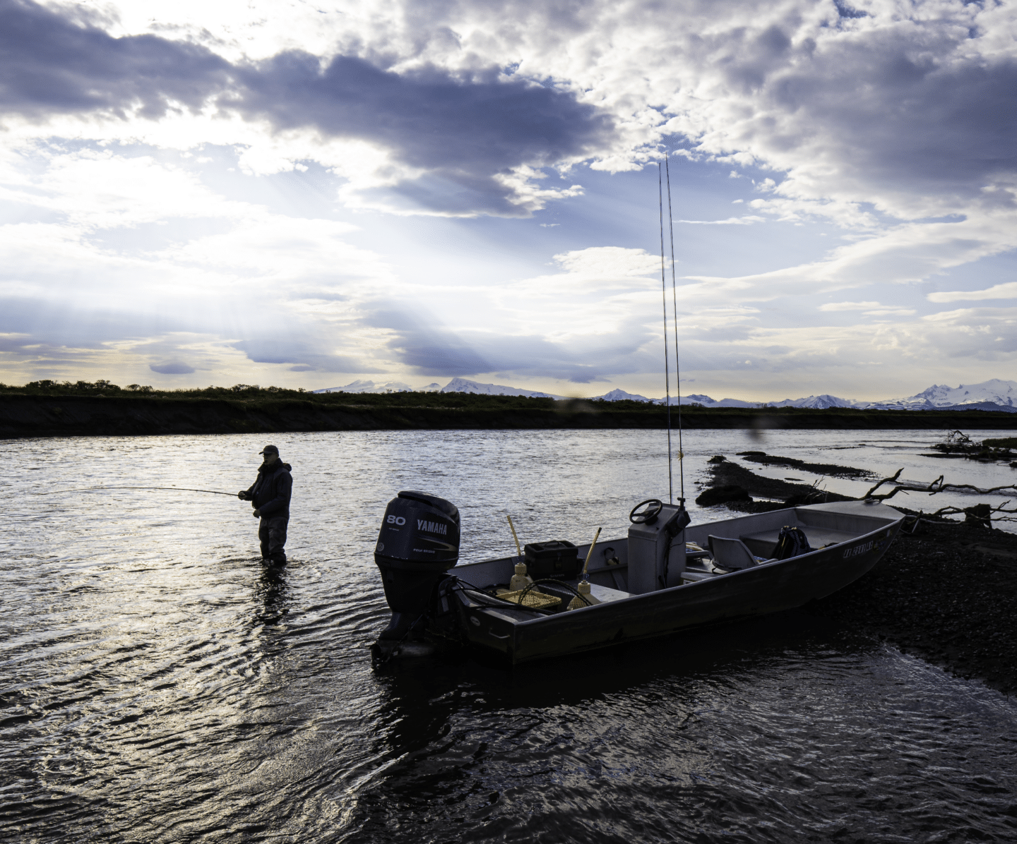 Angler casting line beside boat on Alaska river at sunset