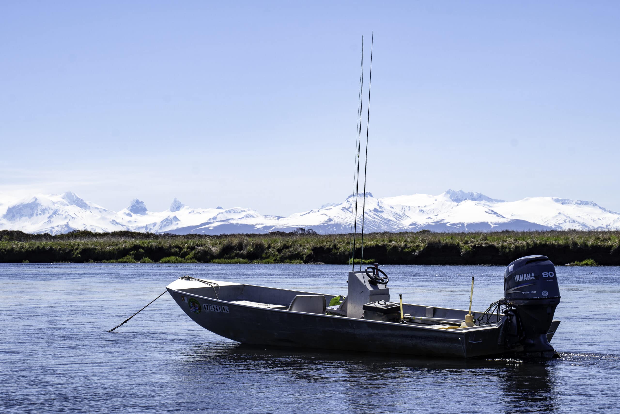 Fishing boat anchored on the river with Alaska’s snow-capped mountains in the background