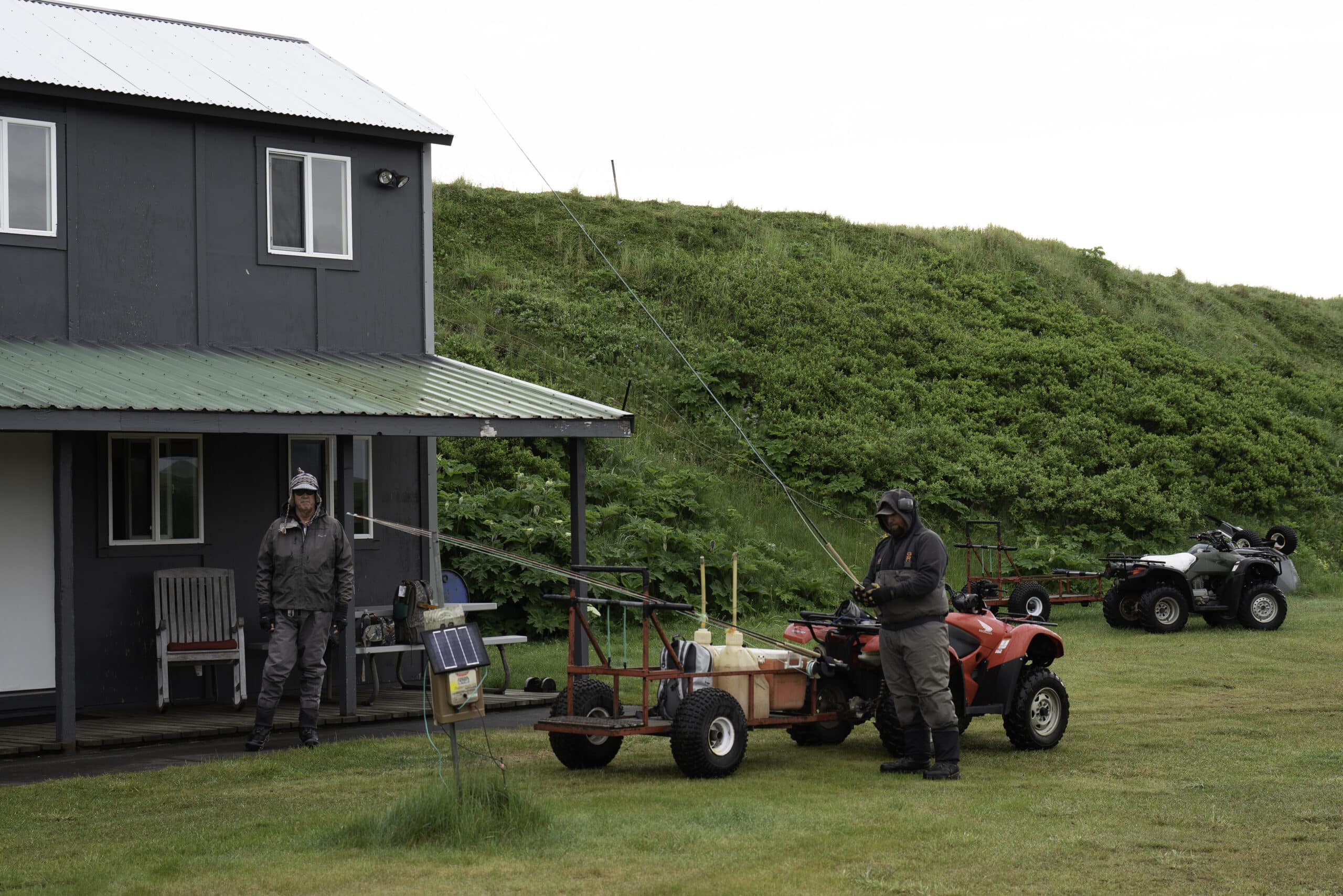 Anglers prepare gear by cabin with ATVs and fishing rods at a remote Alaska river camp