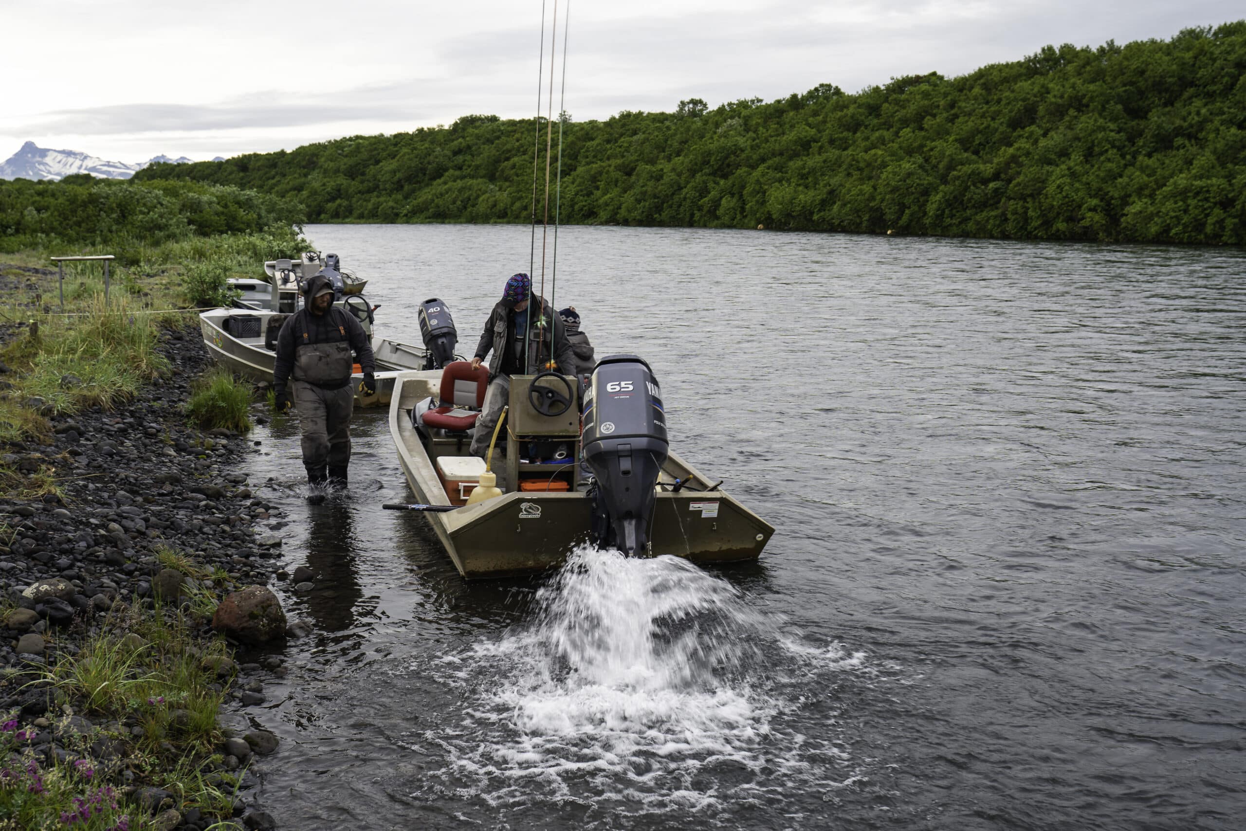 Guides and anglers prepare jet boats along an Alaska riverbank for a remote fishing trip