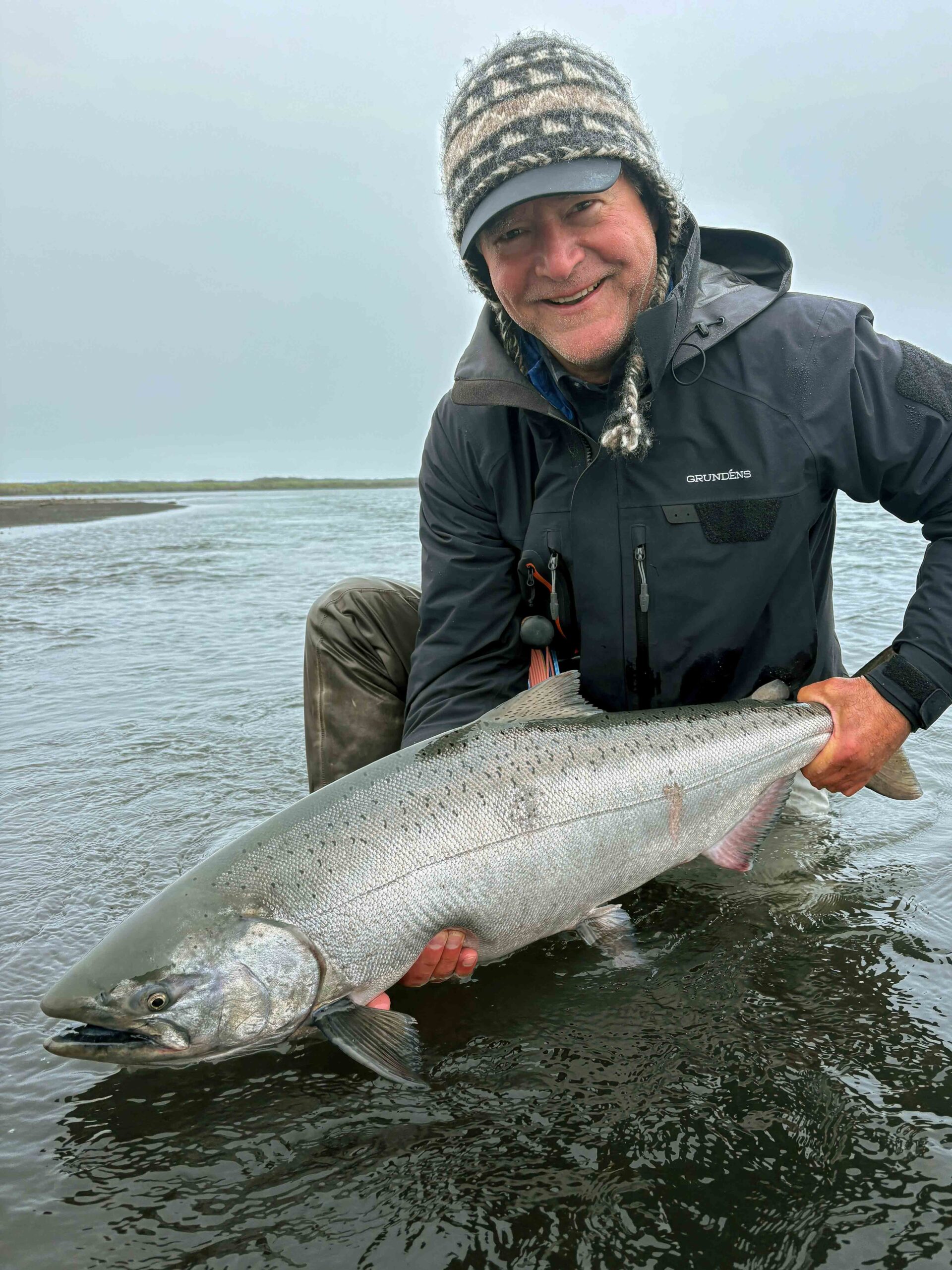 fly angler holding a large king salmon by the riverbank in shallow water