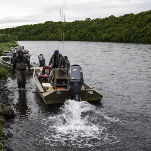 Guides and anglers prepare jet boats along an Alaska riverbank for a remote fishing trip