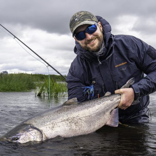 Smiling angler holding a large king salmon caught fly fishing in remote Alaska waters