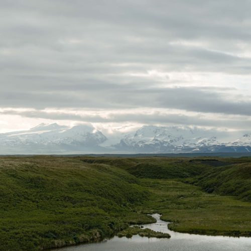 Snow-capped mountains with low clouds above rolling green tundra in Alaska