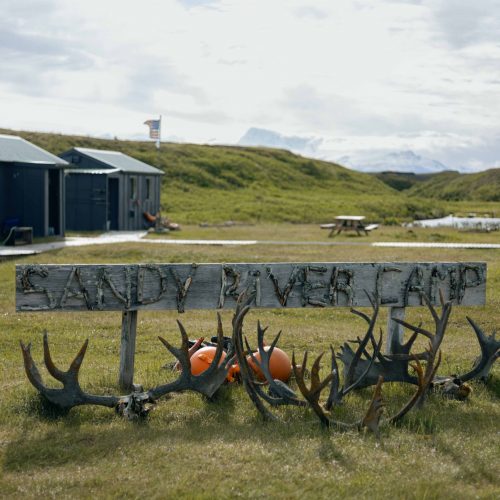 Wooden Sandy River Camp sign decorated with antlers, cabins and tundra in background