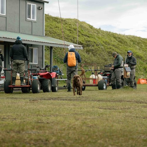 Group of anglers with ATVs and fishing gear preparing outside Alaska river camp lodge