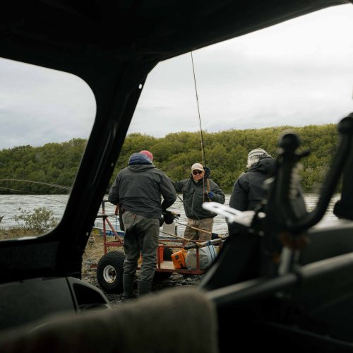 Group of anglers with gear gathered by riverbank, viewed from inside ATV