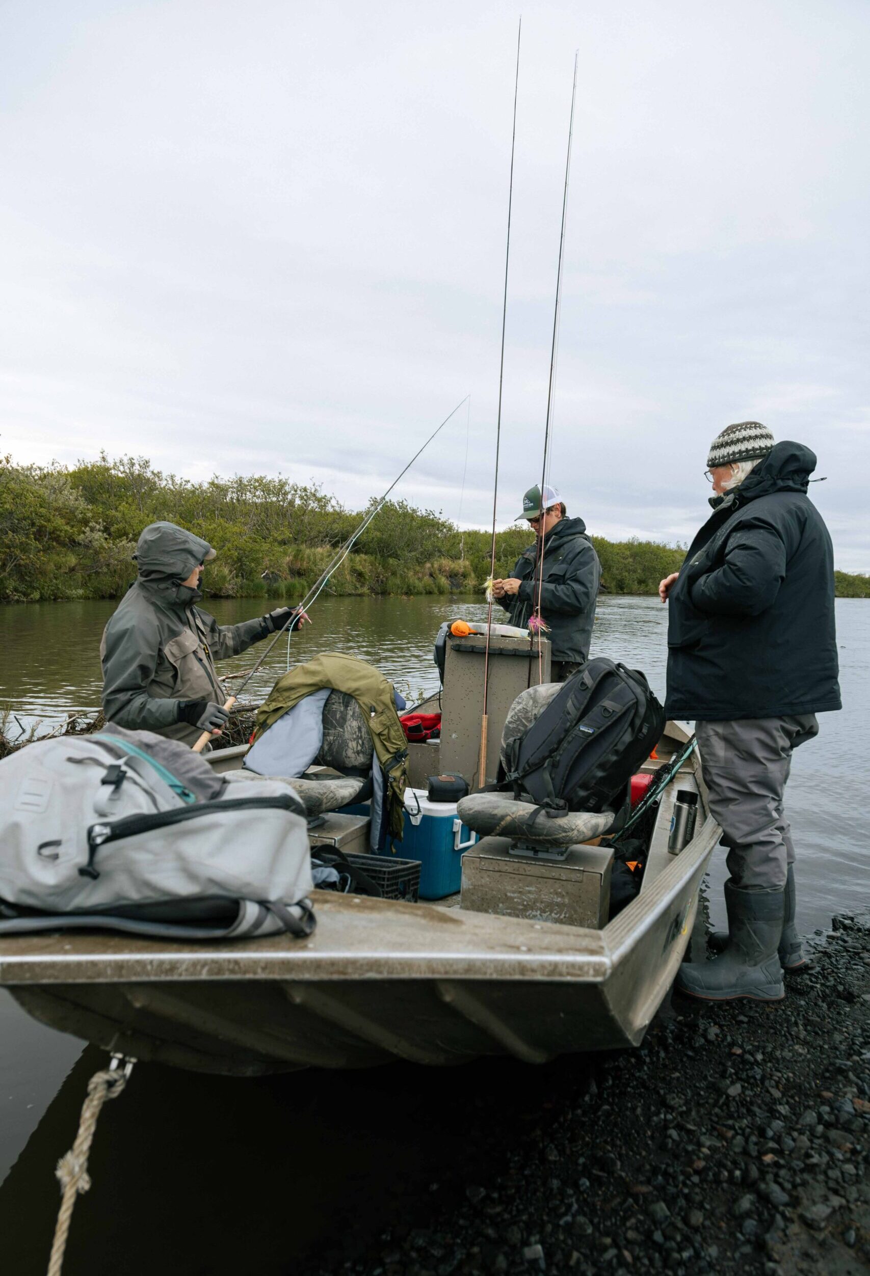 Three anglers preparing fly rods and gear while standing in a boat on the river