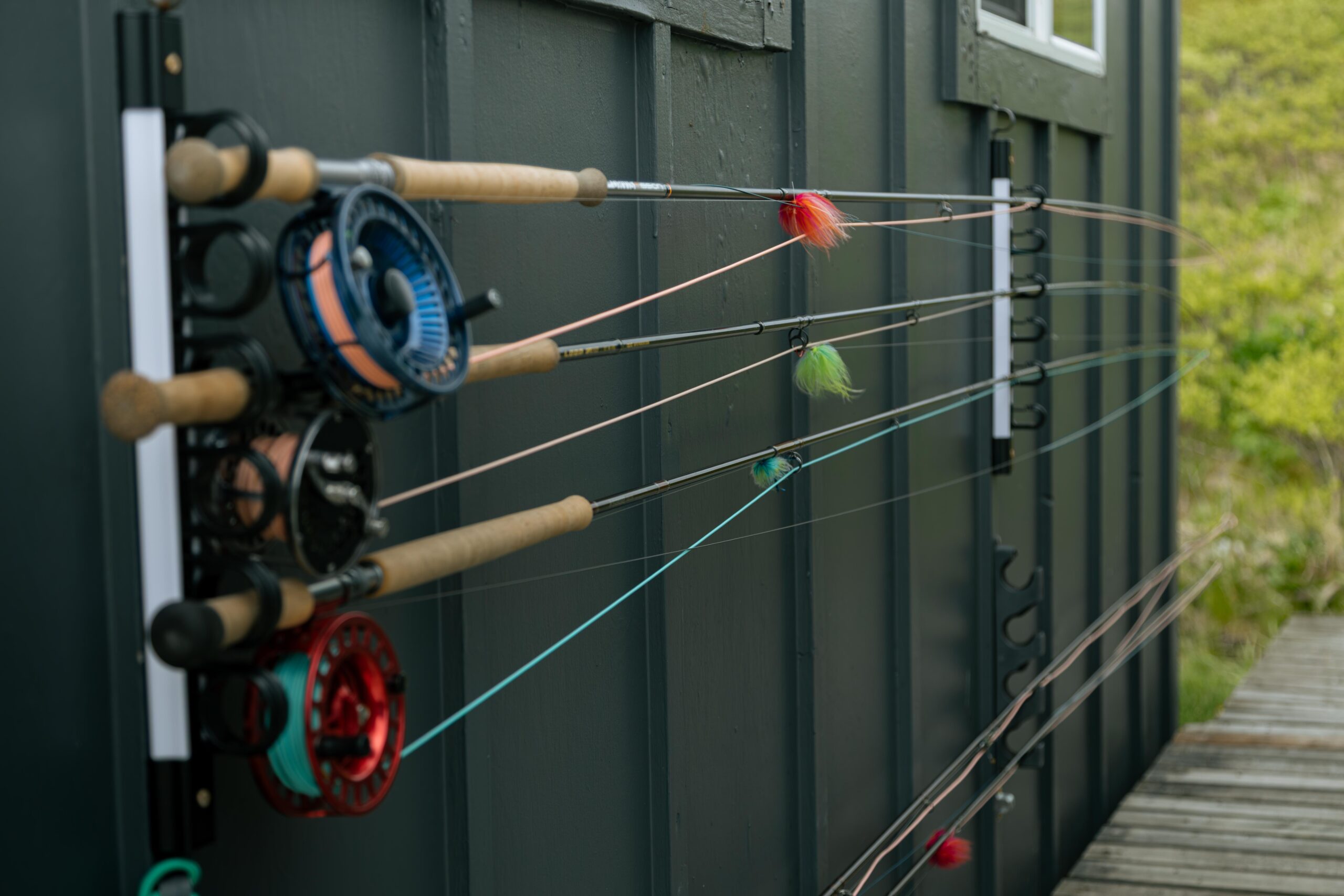 Fly fishing rods with reels and colorful flies stored on outdoor wall rack