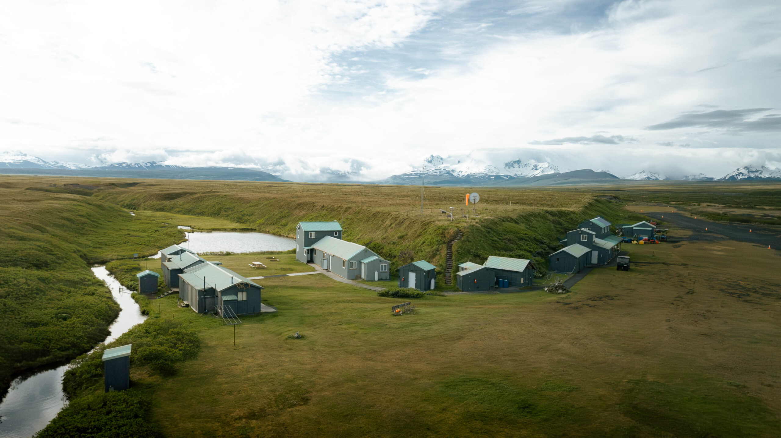 Remote Alaska fishing camp with cabins and outbuildings beside a stream and open tundra