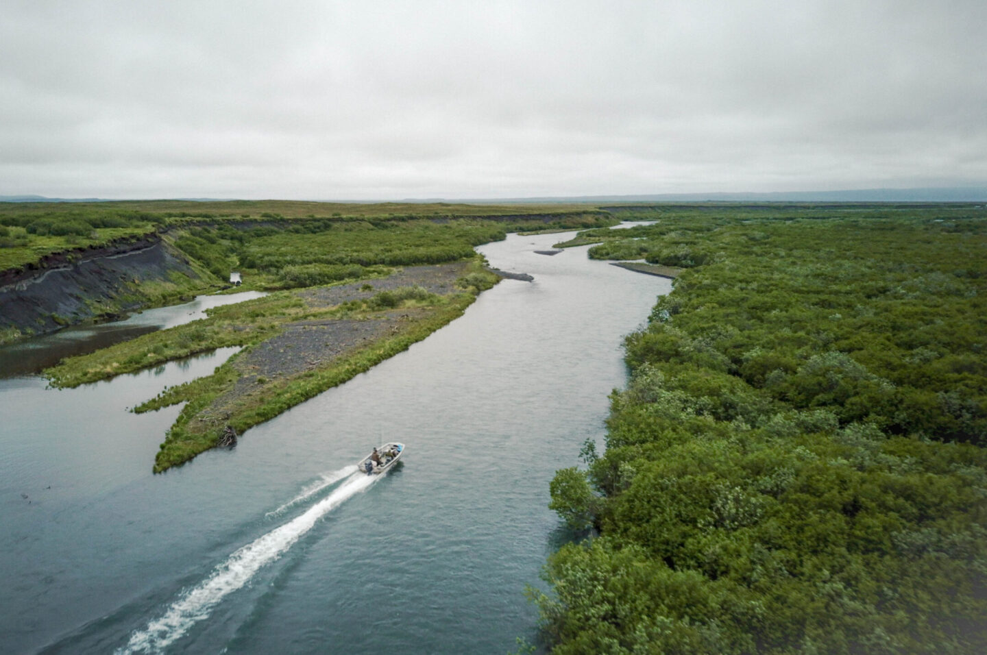 Boat traveling along a winding river surrounded by dense green vegetation under cloudy skies