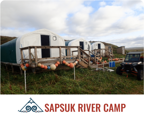 Row of cabins at Sapsuk River Camp, decorated with buoys, with an ATV parked nearby