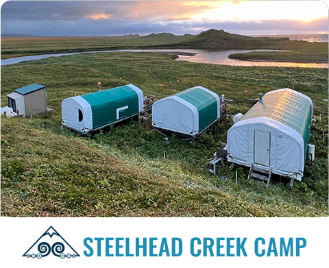 Steelhead Creek Camp with tent cabins on grassy hillside overlooking river at sunset
